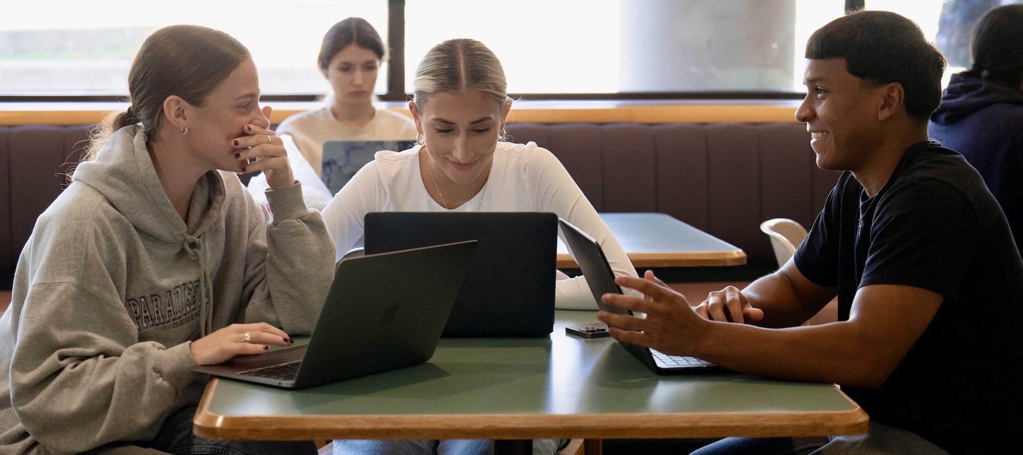 Three students sitting together and laughing at a table in the cafeteria