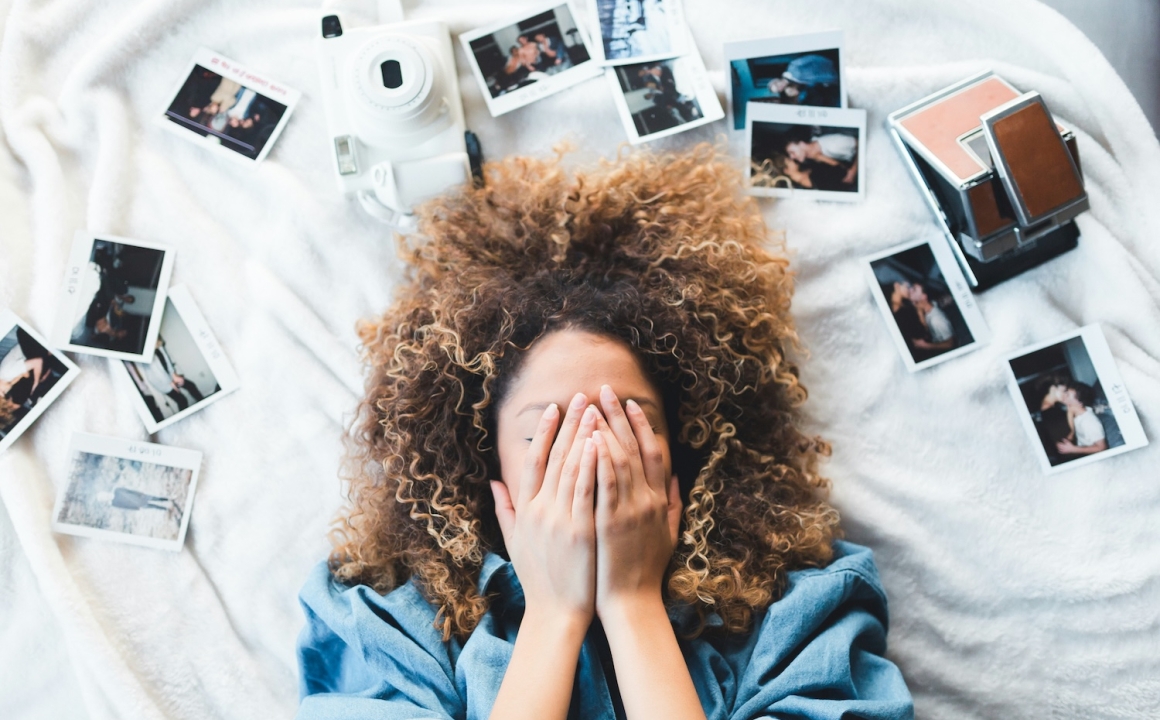A woman laying down with her hands covering in her face in a moment of stress