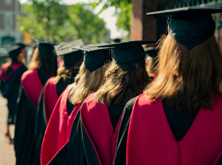 A group of college students in caps and gowns facing away from the camera
