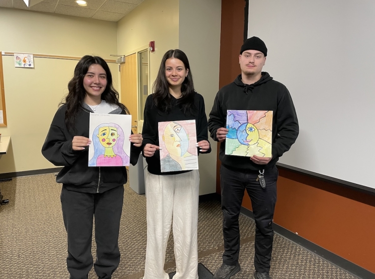 Three HFU students holding up their art projects at the front of a classroom