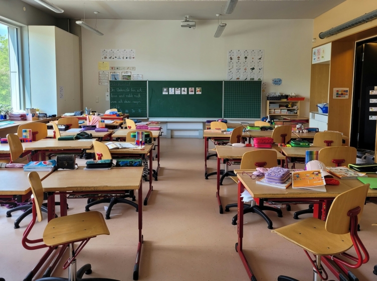 A view from the back of an empty middle school classroom with several desks and a blackboard at the front